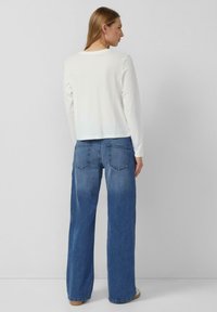 Biała bluzka z długim rękawem w połączeniu z szerokimi niebieskimi dżinsami. Bluzka ma zaokrąglony dekolt, a dżinsy mają klasyczny design pięciu kieszeni.