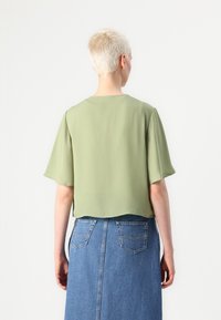 Světlá zelená blůza s krátkým rukávem a volným střihem, s zakřiveným spodním lemem, ve spojení s modrou džínovou sukní s dvěma zadními kapsami.