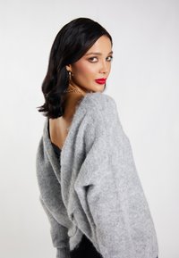 Jasnoszary, oversize sweter wykonany z miękkiego, puszystego materiału z głębokim wycięciem w plecach. Stylizowany na czarną bluzkę, z subtelną teksturą i luźnym krojem.