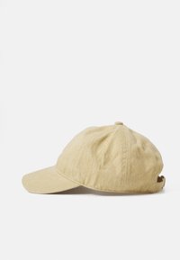Gorra beige hecha de tela texturizada, con un visor curvado, correa ajustable en la parte posterior y orificios de ventilación en los laterales.