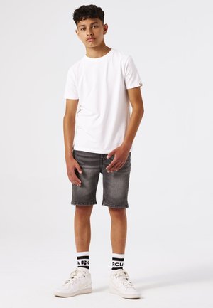 Camiseta blanca de manga corta, pantalones cortos de denim gris, zapatillas blancas y calcetines con patrón en blanco y negro. Diseño minimalista, ajuste casual.