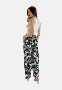 Witte tanktop gecombineerd met zwart-witte broek met bladpatroon, voorzien van een elastische tailleband en een losse pasvorm; lichtgekleurde hakken.