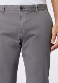 Pantaloni in misto cotone grigi con una consistenza liscia, taglio dritto, chiusura con bottone e tasca frontale con dettagli di cucitura sottili.