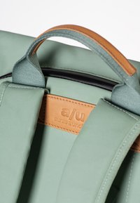 Groene stoffen rugzak met een bruin leren accent, contrasterende stiksels en een bovenhandgreep voor eenvoudig dragen.