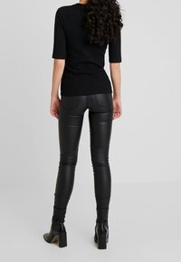 Svart ribbad kortärmad topp i kombination med glänsande svarta faux läderleggings. Leggingsen har bakfickor och en figurnära design.