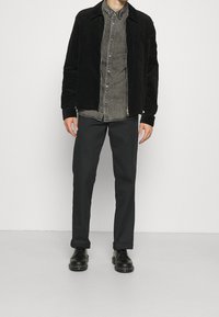 Svart kordflorjacka över en grå skjorta med knappar, tillsammans med mörka byxor och svarta skor. Enkel design, slät textur och inga mönster.