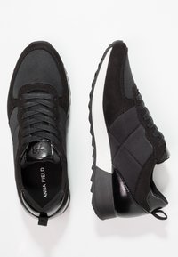 Paire de baskets de sport noires avec dessus en suède et tissu mélangés, lacets noirs, semelles intermédiaires blanches épaisses et semelles extérieures noires texturées.