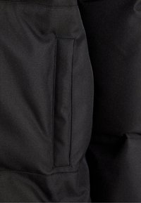 Svart stoff med en teksturert finish, som har en synlig lomme og forsterkede sømmer, noe som indikerer holdbarhet.