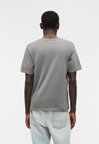 Γκρι μπλουζάκι με κοντά μανίκια, στρογγυλή λαιμόκοψη, άνετη εφαρμογή και εμφανείς ραφές, σε συνδυασμό με ανοιχτό μπλε τζιν παντελόνι.