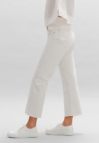 Jeans blancos recortados hechos de mezclilla, con dobladillo deshilachado y diseño clásico de cinco bolsillos, combinados con zapatillas blancas.