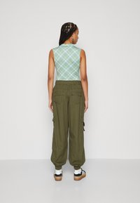 Green and blue plaid sleeveless top paired with loose olive cargo pants; features elastic waist, side pockets, and brown sneakers.