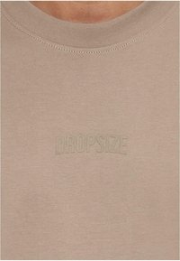 Light beige crew neck T-shirt with a smooth texture and embossed “DROPSIZE” branding on the chest. Simple and fitted design.