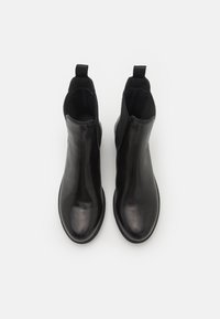 Bottes noires à la cheville avec une finition en cuir lisse, des panneaux latéraux élastiques et des languettes pour un enfilage facile. Semelles en caoutchouc plates et forme épurée.