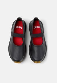 Black leather shoes with a sleek, rounded design, featuring a red interior and a black elastic band across the instep. Light brown rubber sole.