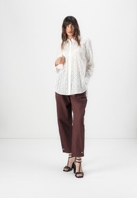Hvit blonde skjorte med knapper og et teksturert mønster, kombinert med mørk maroon vide bukser og svarte stroppete høyhæler. Minimalistisk design.