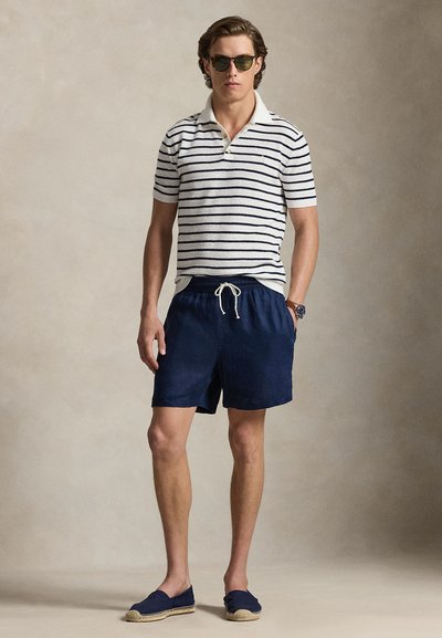 Men's polo shirt with navy and cream stripes, paired with navy shorts and espadrilles. Accessories include dark sunglasses and a wristwatch.