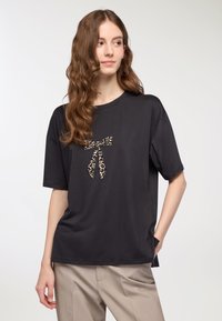 T-shirt nera a maniche corte con un dettaglio a fiocco leopardato sulla parte anteriore. Tessuto morbido, vestibilità rilassata, abbinata a pantaloni color marrone chiaro.