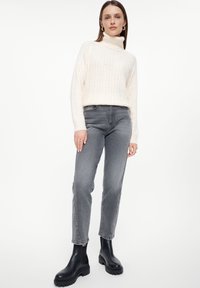 Romantische kabelbreisels turtleneck trui, grijze recht-pas jeans, en zwarte enkellaarsjes. Eenvoudig ontwerp met een gestructureerde afwerking en een getailleerde taille.