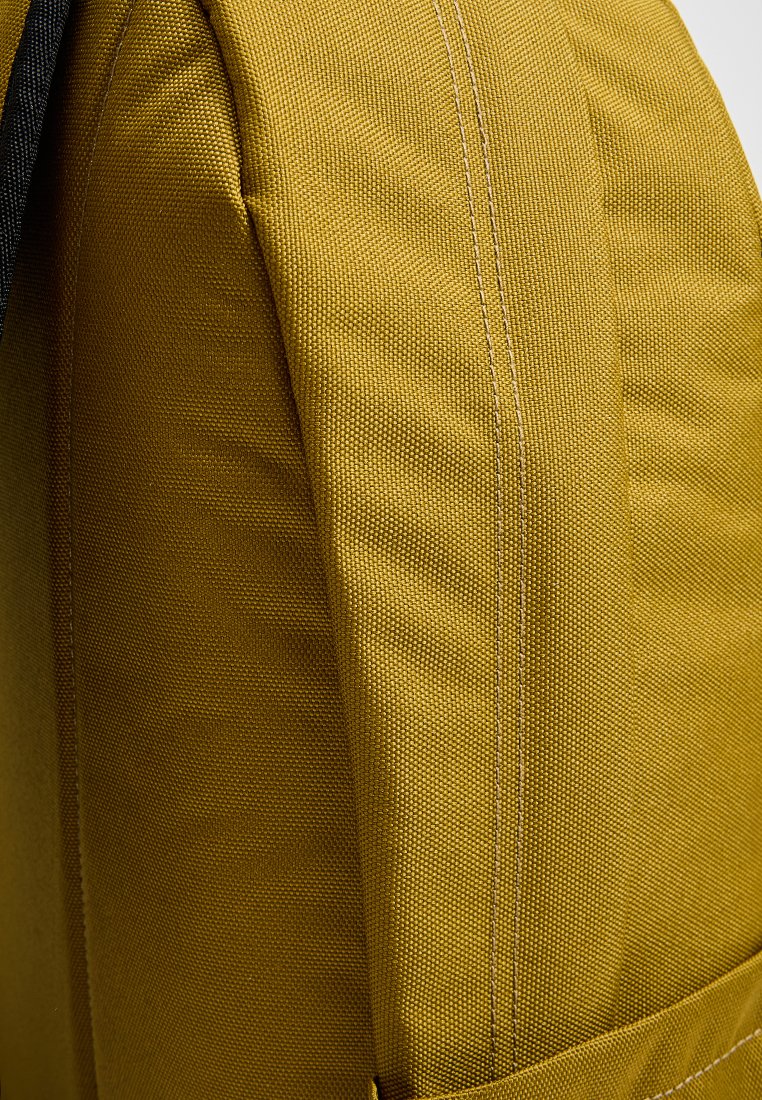 Mochila de tela amarilla con superficie texturizada, costuras prominentes y forma estructurada. Bolsillo lateral visible, que muestra características de diseño prácticas.