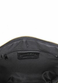 Inuti en svart tygväska med en guldfärgad dragkedja, som har ett litet fack med dragkedja och en texturerad svart lädertagg. Slät yta överlag.