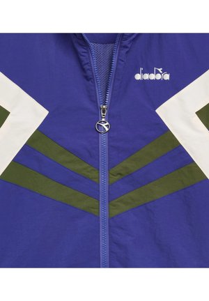 Giacca blu con cerniera frontale, motivi a chevron bianchi e verdi sulle maniche e sul petto, e logo "diadora" sulla parte superiore destra.