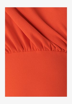 Tela fluida de color naranja con una textura suave. La parte superior tiene detalles fruncidos, que transitan a una sección inferior plana y sin estructura.