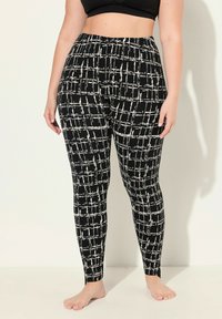 Leggings noirs avec un motif en grille blanche, dotés d'une taille haute, d'une texture lisse et d'un design ajusté, se terminant à la cheville.