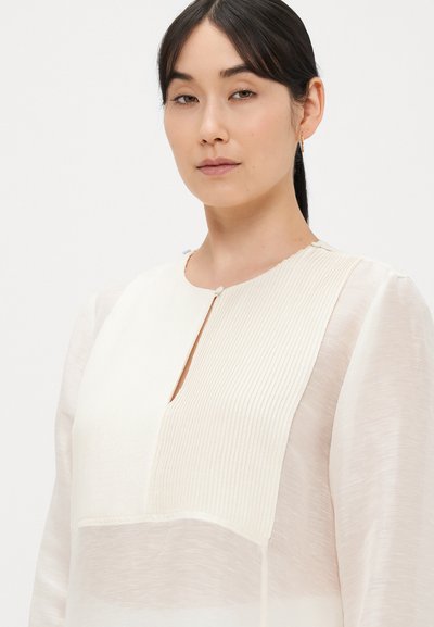 Blusa bianca con pannello frontale intrecciato e strutturato e maniche lisce e trasparenti, con scollo tondo e piccolo dettaglio con bottone al colletto.