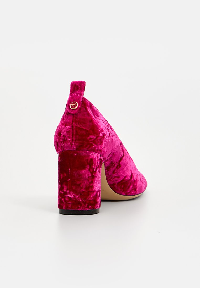 Pump fucsia in velluto con tacco a blocco e punta arrotondata, caratterizzato da un piccolo anello sul retro e un bottone d'accento dorato. Texture liscia.