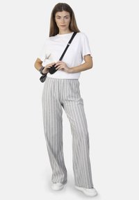 Grijs-witte gestreepte wijde broek van lichtgewicht stof, gecombineerd met een fitted wit t-shirt en witte sneakers, accessoire met een zwarte tas.