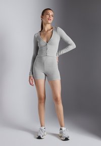 Sivi rebrasti dugorukavi crop top s kopčanjem, uparen s odgovarajućim visokim bokovima šortsevima. Model nosi svijetle atletske tenisice.