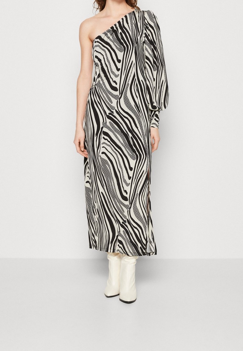 Robe asymétrique à motif zébré, avec des couleurs noir et crème, un tissu fluide et une silhouette ajustée. Accentuée d'une manche volumineuse.
