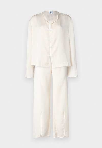 Valge kohev koduriiete komplekt, mis sisaldab lühikest jakk mütsi mandri kollase kaelusega ja sõlme kinnitustega, koos laia säärega pükste ja külgsplitidega.