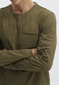 Olíva zöld, hosszú ujjú ing texturált anyagból, mellzsebbe és kerek nyakba szerelve. Slim fit szabás minimális varrásokkal.