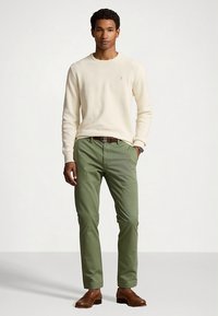 Kremowy sweter dzianinowy, zielone spodnie chino, brązowe skórzane buty. Prosty fason z luźnym krojem i teksturowaną tkaniną. Brak widocznych wzorów.