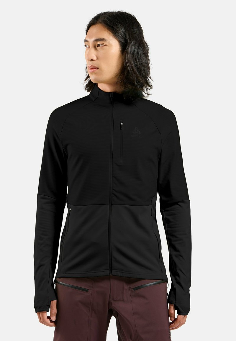 Schwarze Zip-Jacke aus einem glatten, dehnbaren Material. Mit hohem Kragen, Seitentaschen und Daumenöffnungen an den Manschetten.