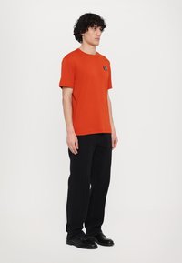 Orange cotton t-shirt with a round neckline and short sleeves, paired with black pants. Simple, unembellished design.