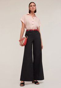 Cămașă roz cu mânecă scurtă și nasturi, pantaloni largi negri cu talie înaltă, curea roșie și sandale negre desluse, purtând o geantă multi-color.