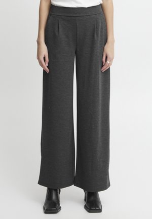 Pantalons larges en tissu gris foncé au toucher lisse, avec une taille plate et des plis ; associés à des bottines noires.