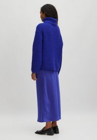 Blue knit sweater with a high collar, paired with a long, solid blue satin skirt and black flat shoes. Textured fabric, loose fit.