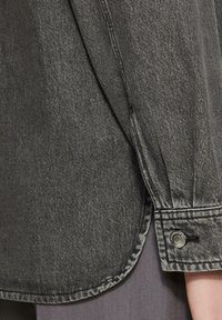 Ciemnoszara koszula dżinsowa z rękawem i mankietem, ozdobiona detalem guzika i kontrastowym przeszyciem. Teksturowany materiał z lekko zużytym wykończeniem.