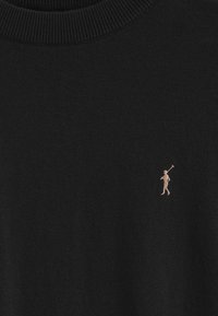 Svart stickad tröja med ribbad krage, prydd med en liten beige broderad polo-spelare-logotyp på bröstet. Mjuk textur, avslappnad design.