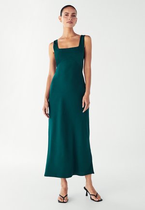 Long, solid dark green dress with a square neckline, slim fit, and smooth texture. Model wearing black heeled sandals.