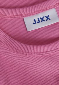 Roze ribstof van een kledingstuk met een ronde halslijn. Het label heeft "JJXX" in het blauw, dichtbij de halsnaad geplaatst.
