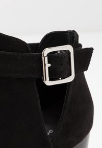 Närbild av svart mockaskosnör med silverfärgad rektangulär spänne mot en vit bakgrund.