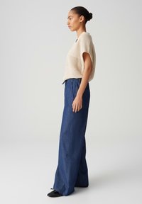 Beige knit top with short sleeves paired with wide-leg blue denim pants. The pants feature an elastic waistband and side pockets.