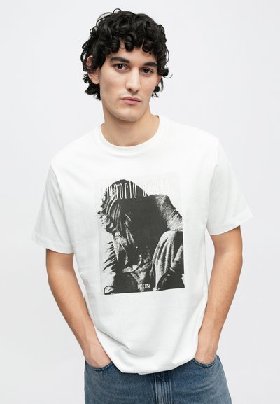 Λευκό βαμβακερό μπλουζάκι με μαύρο και άσπρο γραφικό τύπωμα καθιστής φιγούρας. Κοντά μανίκια και στρογγυλή λαιμόκοψη. Κλασική εφαρμογή.