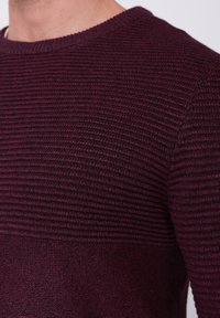 Pull bordeaux avec des motifs en côtes texturées et en maille lisse, col rond et coupe ajustée, présentant un dégradé de couleurs riche.