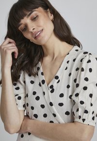Vestido blanco con lunares negros, mangas cortas abullonadas y escote en V. Tejido texturizado con un acabado suave para un detalle adicional.