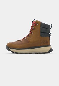 Botte de randonnée imperméable marron avec un col en feutre gris, des lacets rouges, des œillets en métal et une semelle noire crantée pour une meilleure traction. Présence d'un logo sur le côté.
